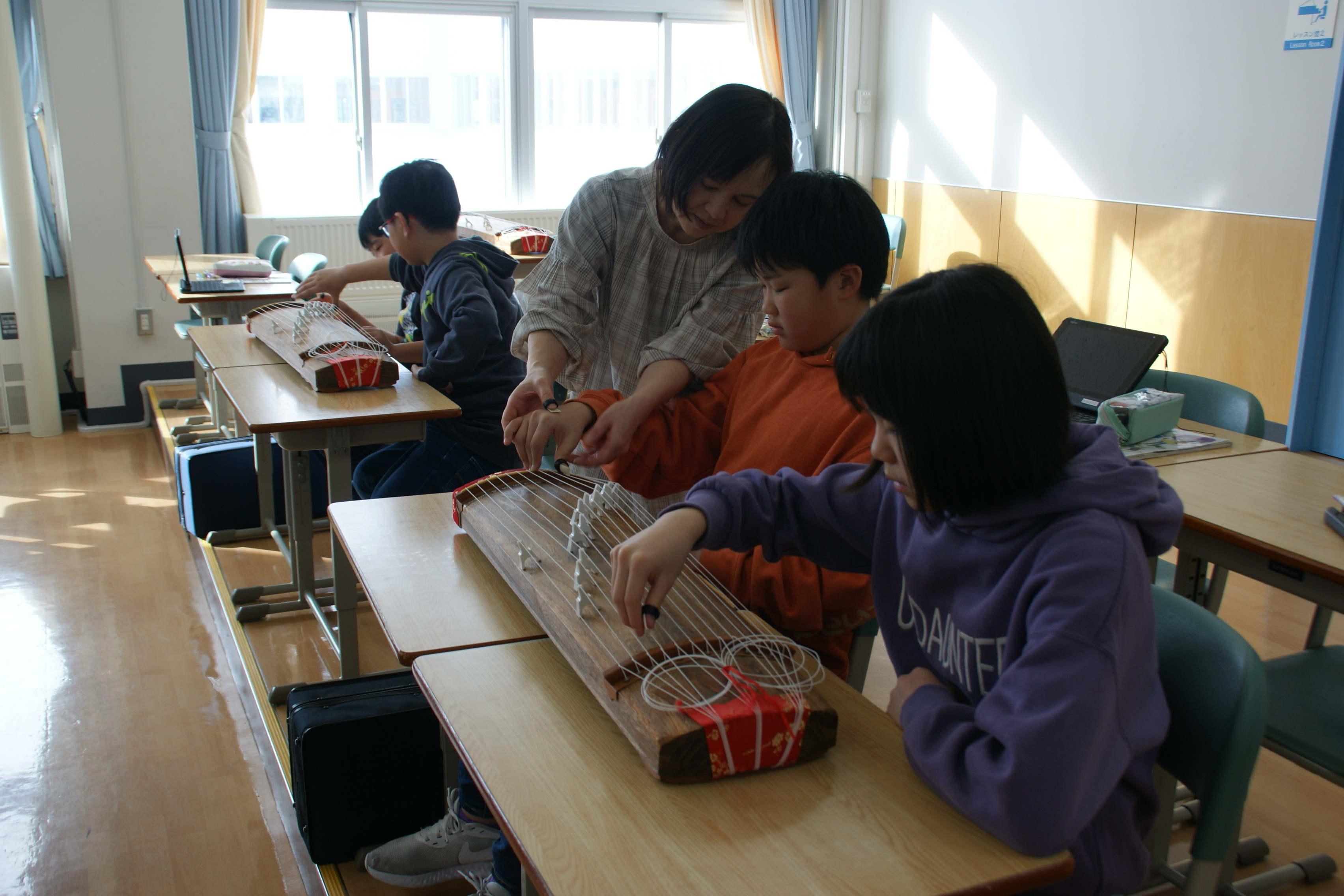 小学生に琴を指導する中学校の音楽教員