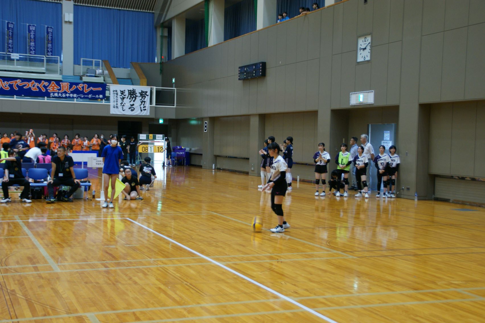 サーブを打つ選手と応援する選手たち.JPG